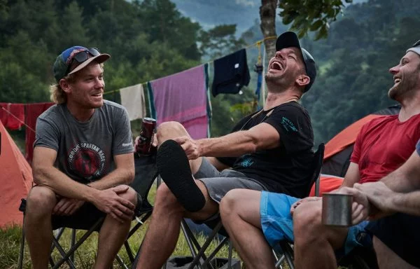 Solo adventure travellers laughing around a campfire with drinks in hand