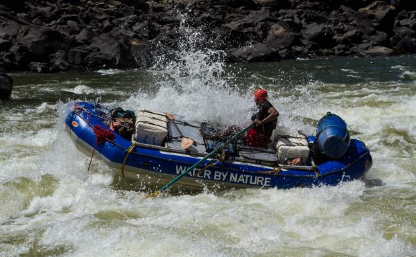 A blue oar boat navigates the rapids