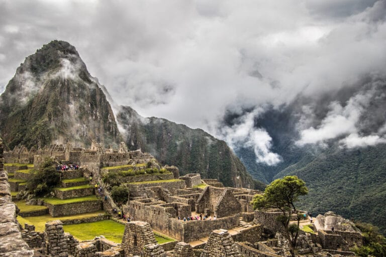 View of Machu Picchu’s ancient stone ruins nestled high in the Andes Mountains, with dramatic green peaks and mist rolling through the valley.
